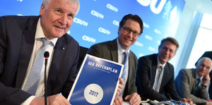 Horst Seehofer hält ein Heft mit der Aufschrift „Bayernplan“ in der Hand. Neben ihm sitzen weitere Politiker