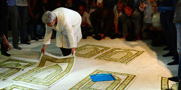 Eine Frau in weißem Gewand legt einen Gebetsteppich in der Moschee bereit