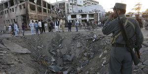 Menschen vor einem Bombenkrater und völlig zerstörten Häusern in Kabul