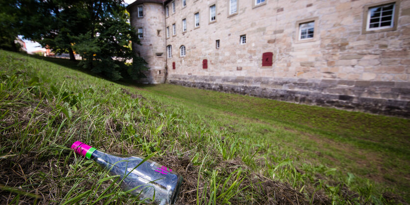 Auf einer Wiese vor einem Schloss liegt eine leere Flasche