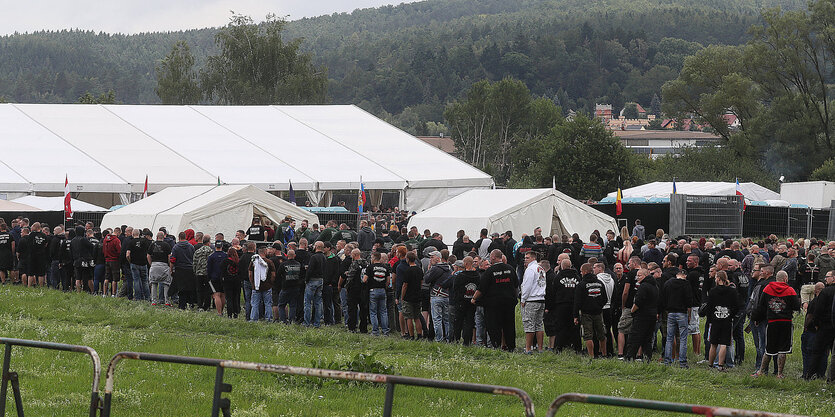 Zahlreiche Personen stehen Schlange, um in ein weißes Zelt zu gelangen Davor stehen Absperrungen