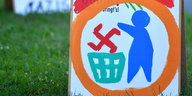 ein handgemaltes Schild, auf dem ein Männchen ein Hakenkreuz in eine Mülltonne wirft