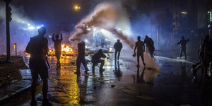 Menschen werfen nachts Steine vor brennenden Barrikaden