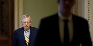 rechts ein Mann unscharf im Vordergrund, links ein Mann in Anzug mit Brille und gelber Krawatte, es ist der Mehrheitsführer der Republikaner im US-Senat Mitch McConnell