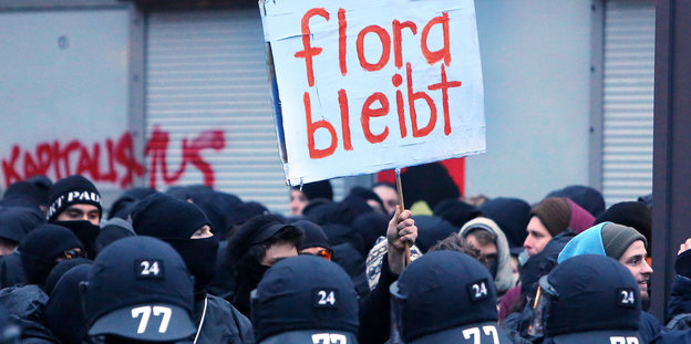 Viele Polizisten vor Demonstranten, die ein Schild mit der Aufschrift "Flora bleibt" halten