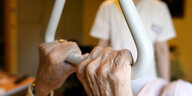 Eine Seniorin hält sich in ihrem Bett an einem Haltegriff fest, im Hintergrund ein Pfleger
