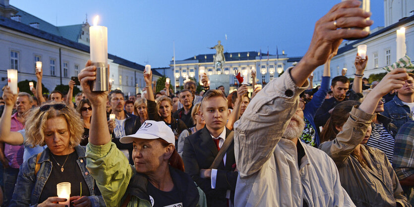 Menschen stehen auf einem Platz und halten Grabkerzen in die Höhe. Es dämmert.