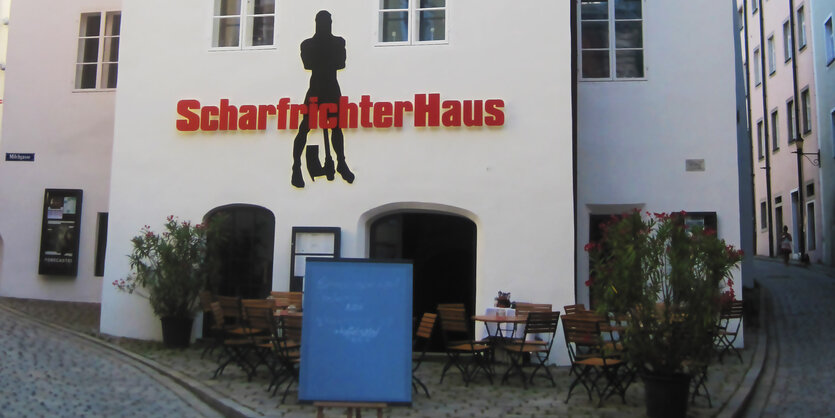 Auf einer Fassade steht „Scharfrichterhaus“. Davor sind Tische und Stühle aufgestellt