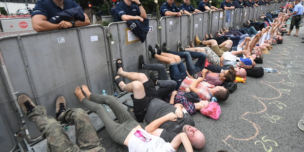 Menschen liegen auf dem Boden und trampeln mit den Füßen gegen eine Absperrung