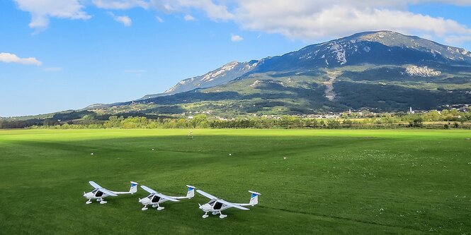 Drei Flugzeuge stehen auf einer Wiese nebeneinander. Im Hintergrund ein Berg