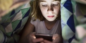 Ein Mädchen tippt unter der Bettdecke auf dem Smartphone rum