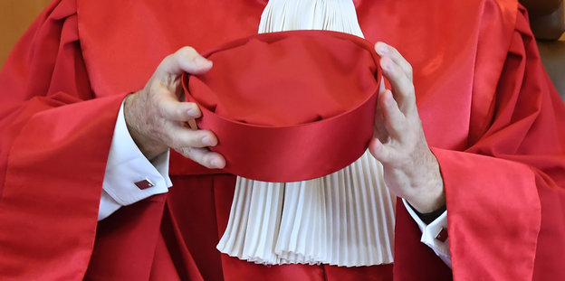 Ein Mensch mit rotem Gewand hält eine rote Kappe in den Händen
