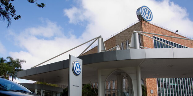 Einfahrt zu einer Fabrik auf deren Dach ein großes VW-Zeichen steht