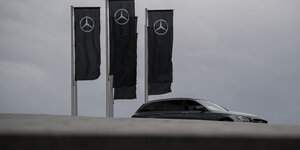 Ein schwarzes Auto fährt vor trübem Himmel unter drei schwarzen Mercedes-Flaggen vorbei