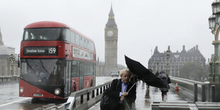 Ein Mann mit einem Regenschirm geht am 06.06.2017 auf der Westminister Bridge in London (Großbritannien) im Regen entlang einer Absperrung, im Hintergrund ist ein roter Doppeldeckerbus zu sehen.