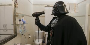 Ein Mann im Kostüm von Darth Vader hält einen Föhn