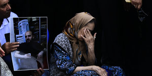 Ein kniende Frau hält sich eine Hand vor das Gesicht. Daneben Menschen mit Plakaten