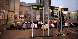 Eine Männergruppe betet, vor der ihr stehen Metallstangen