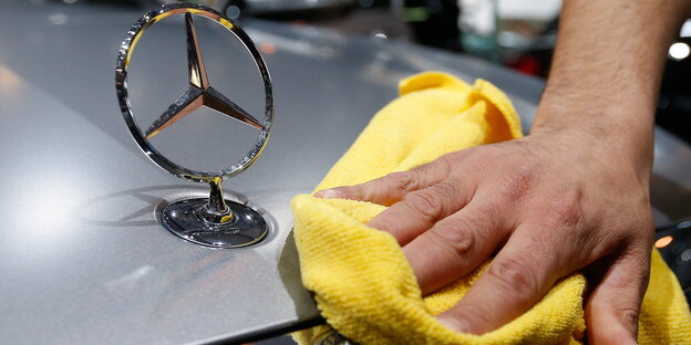 Eine Hand wischt mit einem gelben Tuch über die Motorhaube eines Mercedes