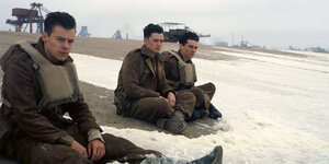 Drei junge Männer in Uniform sitzen am Strand