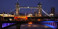 Ein roter Doppeldeckerbus fährt über eine Londoner Brücke in der Nacht