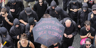 Schwarz gekleidete DemonstrantInnen tragen einen Regenschirm, auf dem steht: „Ich distanziere mich von der Gewalt der Polizei“