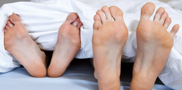 Zwei Paar Füße gucken unter einer Bettdecke hervor