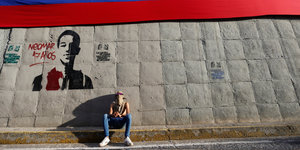 Ein vermummter sitzt unter einem Graffito