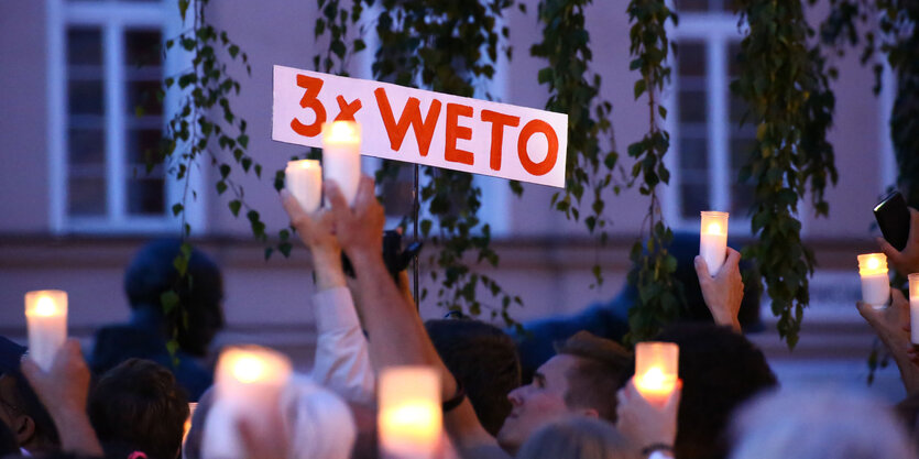 Menschen halten Kerzen und ein Schild in die Höhe