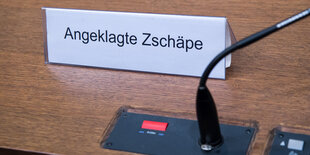 Neben einem Tischmikrofon ein Platzschild mit der Aufschrift „Angeklagte Zschäpe“