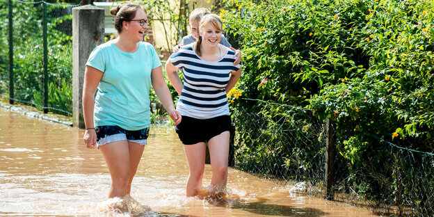 Frauen laufen mit einem Kind auf dem Rücken durchs Wasser Frauen laufen mit einem Kind auf dem Rücken durchs Wasser
