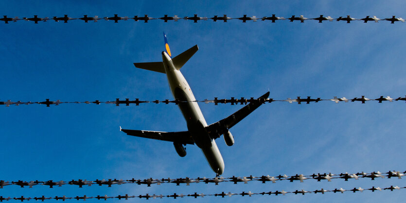 Ein Flugzeug fliegt über einen Stacheldrahtzaun