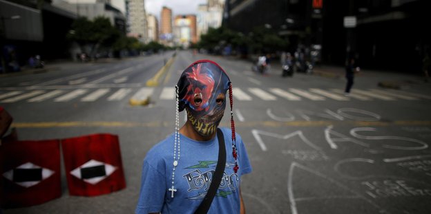 Ein maskierter Mann mit Rosenkränzen steht auf einer leeren Straße