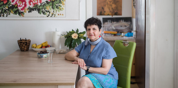 eine Frau, Emel Zeynelabidin, sitz an ihrem Küchentisch und lächelt in die Kamera