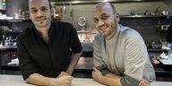 Zwei Männer, die Zwillinge Thomas und Mathias Sühring, stehen mit den Armen auf einen Tisch gelehnt in ihrer Küche