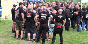 Kräftig gebaute Männer in schwarz-weiß-roten Band-T-Shirts stehen auf einer Wiese