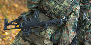 Ein Soldat in Tarnuniform ist von hinten zu sehen, um seine Hüfte hängt eine schwere Waffe
