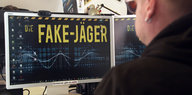 Ein Mann sitzt vor einem großen Computer-Bildschirm, auf dem in gelber Schrift "Fake-Jäger" steht