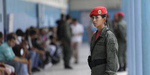 Eine Soldatin mit rotem Barett steht in einem Gang, hinter ihr sitzen wartende Menschen