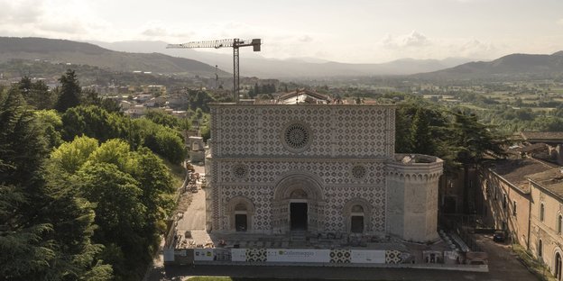 Luftbild der Basilica di Santa Maria di Collemaggio in L'Aquila - im Hintergrund ein Baukran