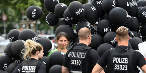 Polizisten stehen vor einer Frau mit vielen schwarzen Luftballons mit der Aufschrift NOx