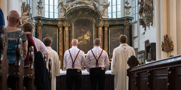 Zwei Männer stehen mit zwei Pfarrern vor einem Altar