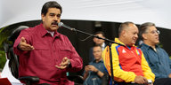 Ein Mann in einem roten Hemd an einem Mikrofon, weitere Männer im Hintergrund