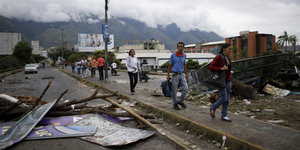 Fußgänger laufen in Caracas an einer Barrikade vorbei, im Hintergrund Berge und Wolken