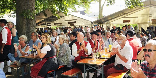 Etliche Menschen sitzen an Bierbänken und klatschen