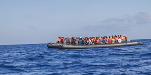 ein großes Schlauchboot voller Menschen, von denen die meisten Schwimmwesten tragen