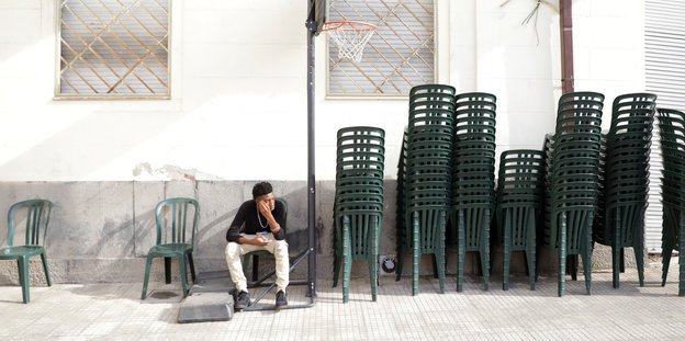 Ein Mann sitzt auf einem Plastikstuhl neben aufgetürmten Plastikstühlen