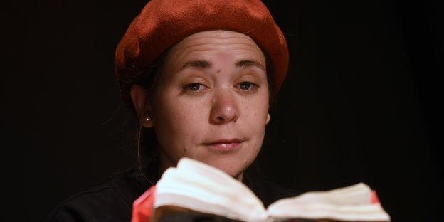 Stefanie Sargnagel mit roter Mütze, ihrem Markenzeichen, und einem Buch bei einer Lesung
