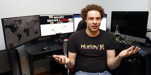 Mann mit Afro, im Hintergrund ein Schreibtisch mit vier Monitoren