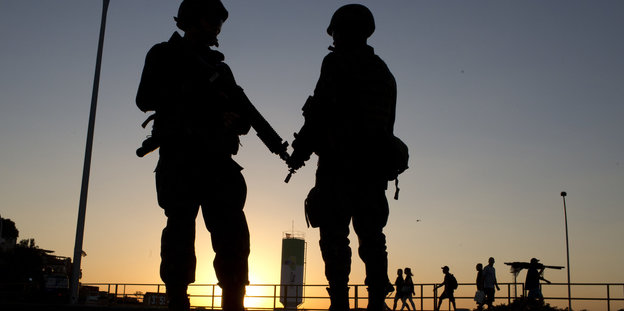 Im Hintergrund der Sonnenuntergang, im Vordergrund das Profil zweier Soldaten